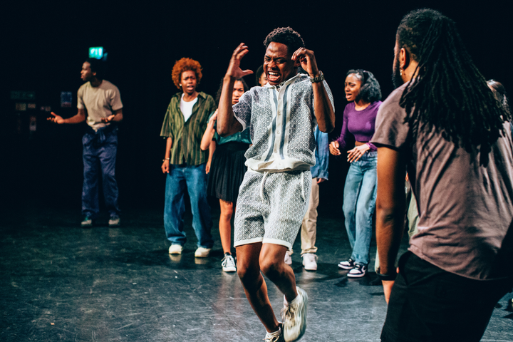 Actor dances on stage in a matching two-piece set surrounded by other actors on the Originate course.