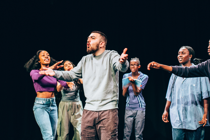 An Originate student acts passionately centre stage while other students extend their arms towards the actor.