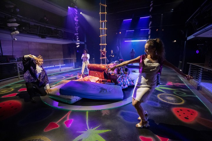 Actors dancing joyously on stage with bright stage lighting in bright blue, green and pink