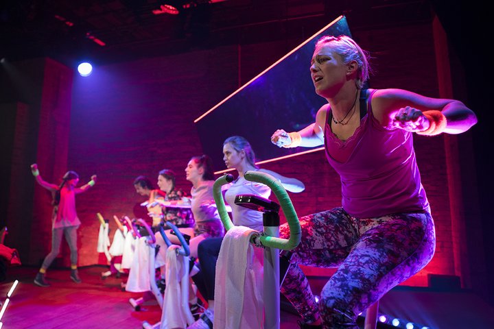 Festival 2018 photo in neon colours including pinks and purples with women sitting on spin bicycles