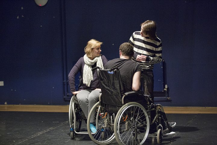 A group workshop featuring disabled and non-disabled people acting in a blue and black theatre space.