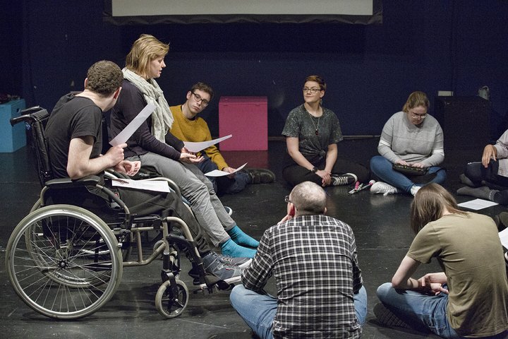 A group workshop featuring disabled and non-disabled people acting in a theatre space.