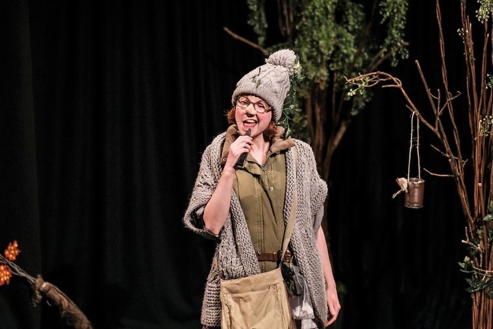 Actress Clare-Louise English on stage at RADA in woodland set with woolly hat, comical glasses and nose