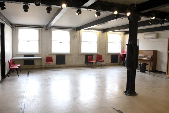 Empty Ellen Terry studio with four big windows, red chairs around the edges and an upright piano
