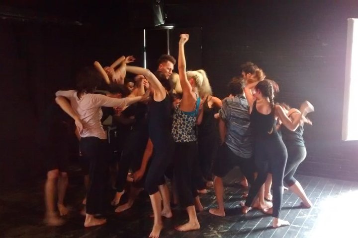 A group of students in a movement workshop moving in a tight group in a small brick-walled studio
