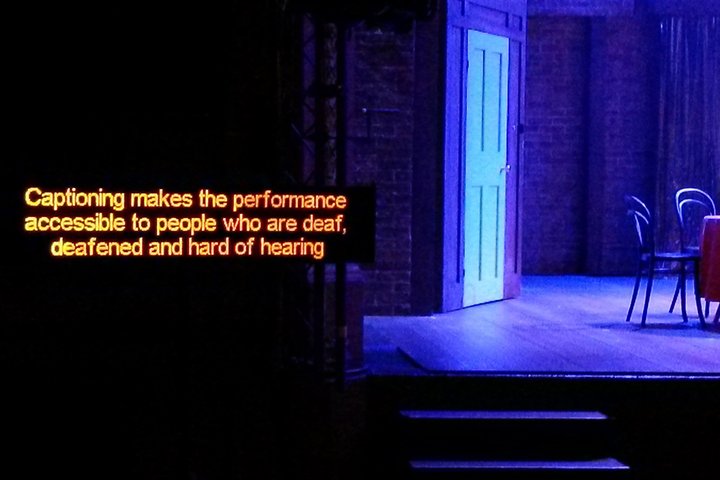 A caption screen next to an empty blue-lit stage.