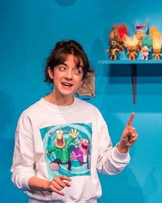 Patsy Ferran gesturing on stage in My Mum's A Tw*t at the Royal Court Theatre; set of a child's bedroom with bright turquoise wall.
