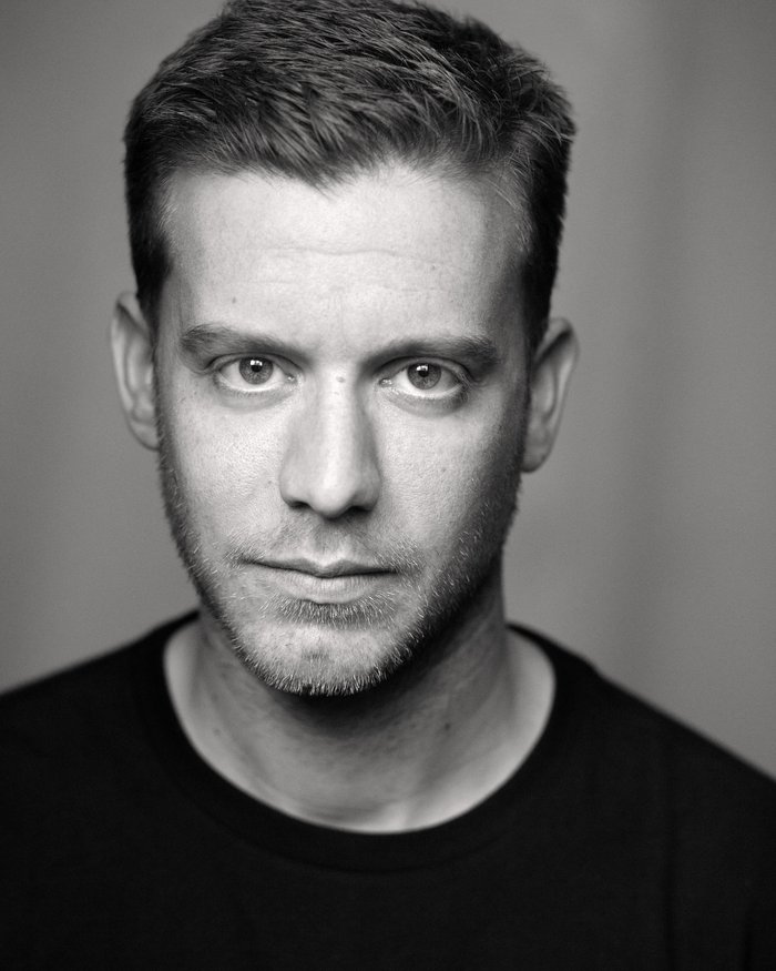 Profile of an actor looking directly at the camera in dark clothing.