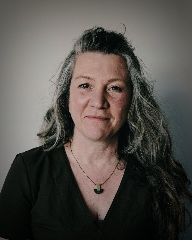 Head and shoulders image of Rachel Nicholson smiling directly at the camera in dark lighting