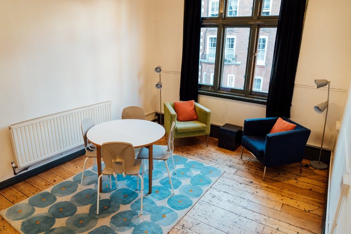 A medium sized room with wooden floors. There are two arm chairs and a table.