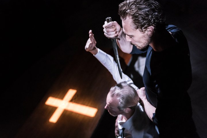 Tom Hiddleston as Hamlet holds a dagger above Nicholas Farrell as Claudius who is praying in a scene from Hamlet