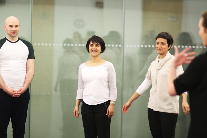 Three Short Course participants stand in a semi-circle as part of a warm-up exercise. They are smiling.