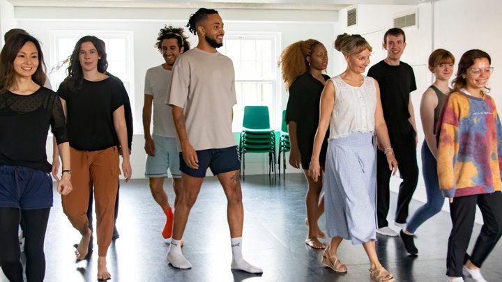 A diverse and smiling group of actors walk around a rehearsal room