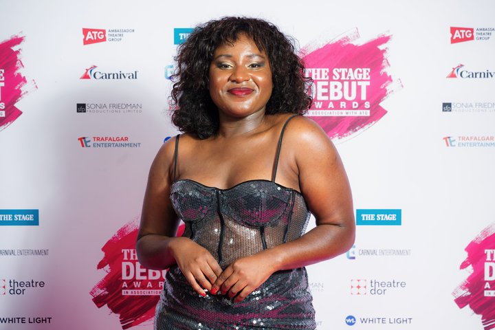 BA acting graduate Susan Wokoma stands in front of The Stage branded wall smiling