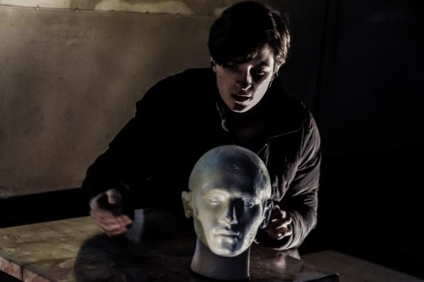A performer leans towards a microphone shaped as a human head in a performance of Thrown
