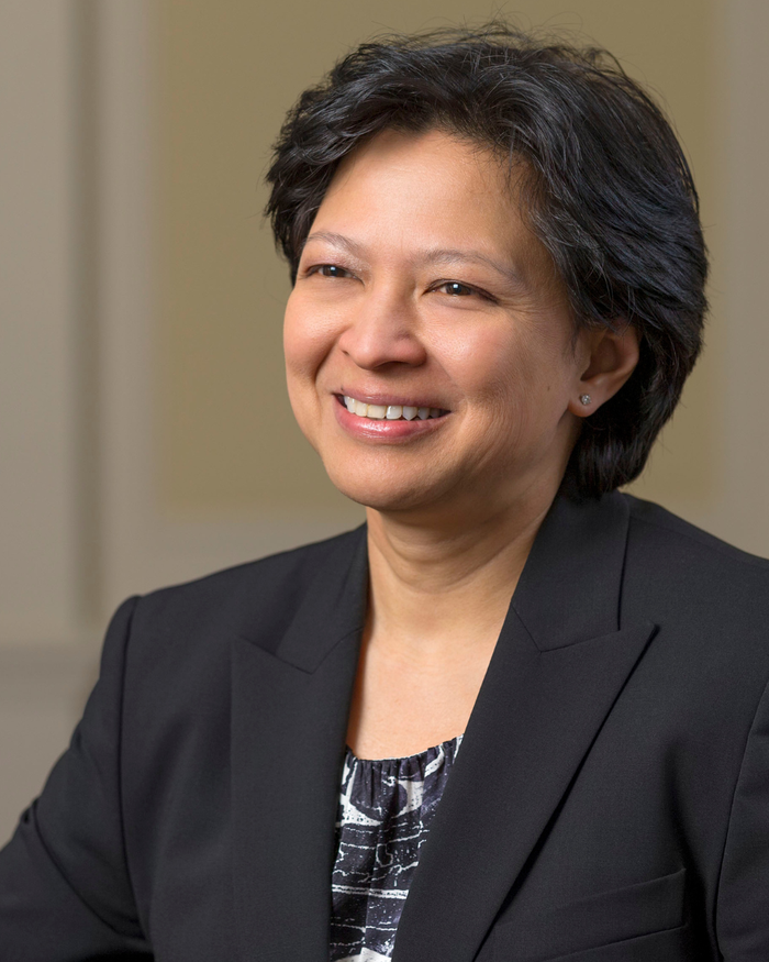 Judith Chan sits at a diagonal angle to the camera, smiling brightly wearing a black suit jacket.