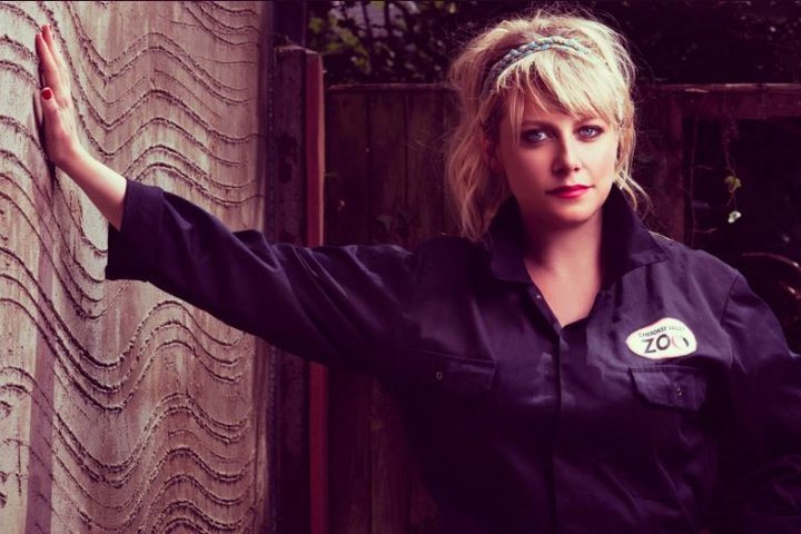 Lily Bevan stands leaning against a wall in overalls in a promo shot for Zoo