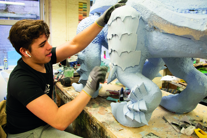 In the props workshop at RADA, a male theatre production student works on sculpting the scales of a model sea monster for a props project