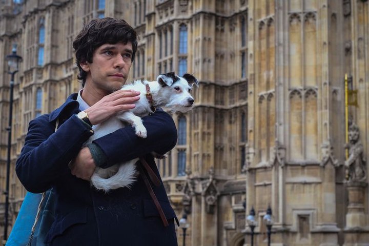 © BBC A scene from BBC's A Very English Scandal. Ben Whishaw, looking pensive, stands in front of the Houses of Parliament holding a scruffy white terrier.