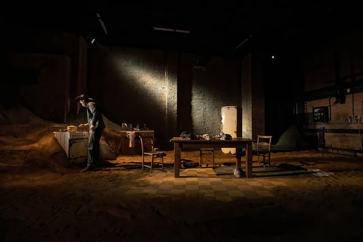 An actor cooks in dramatic lighting, in an apocalyptic kitchen featuring rusted appliances.