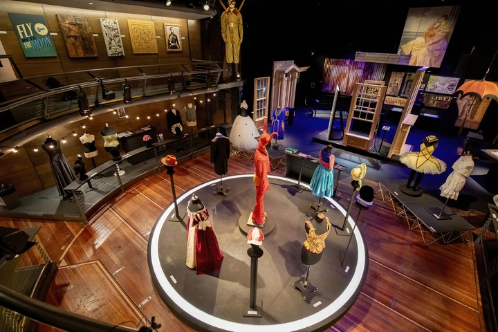 Wide shot of Production Exhibition showing exciting and bright costumes, props, scenic art and construction in an epic theatre setting.