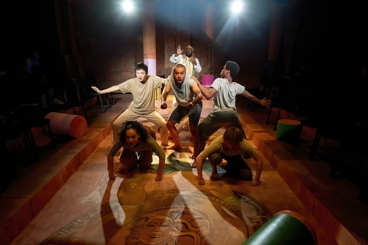 © Linda Carter Eight students perform on stage in dramatic lighting. The image is energetic with students braced in a chariot formation.
