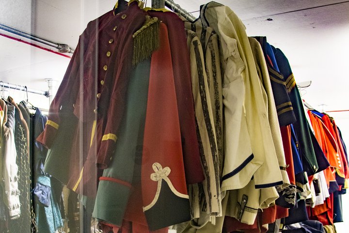 A rail of theatrical costumes, primarily red, cream and blue military jackets with gold buttons and fringing