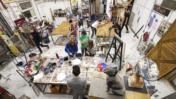 A birds eye view of a busy scenic art workshop, with students mixing paint and working on creating a replica parquet floor