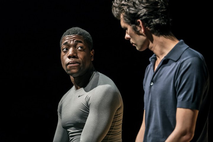 © RADA graduate and actor Fehinit Balogun sits on stage in conversation with Ben Whishaw in a scene from Against at the Almeida Theatre